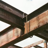 Close-up of rusty steel beams and chains in outdoor industrial construction site.